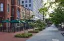 A tree-lined brick sidewalk in downtown Washington, DC, with green café umbrellas over outdoor tables.