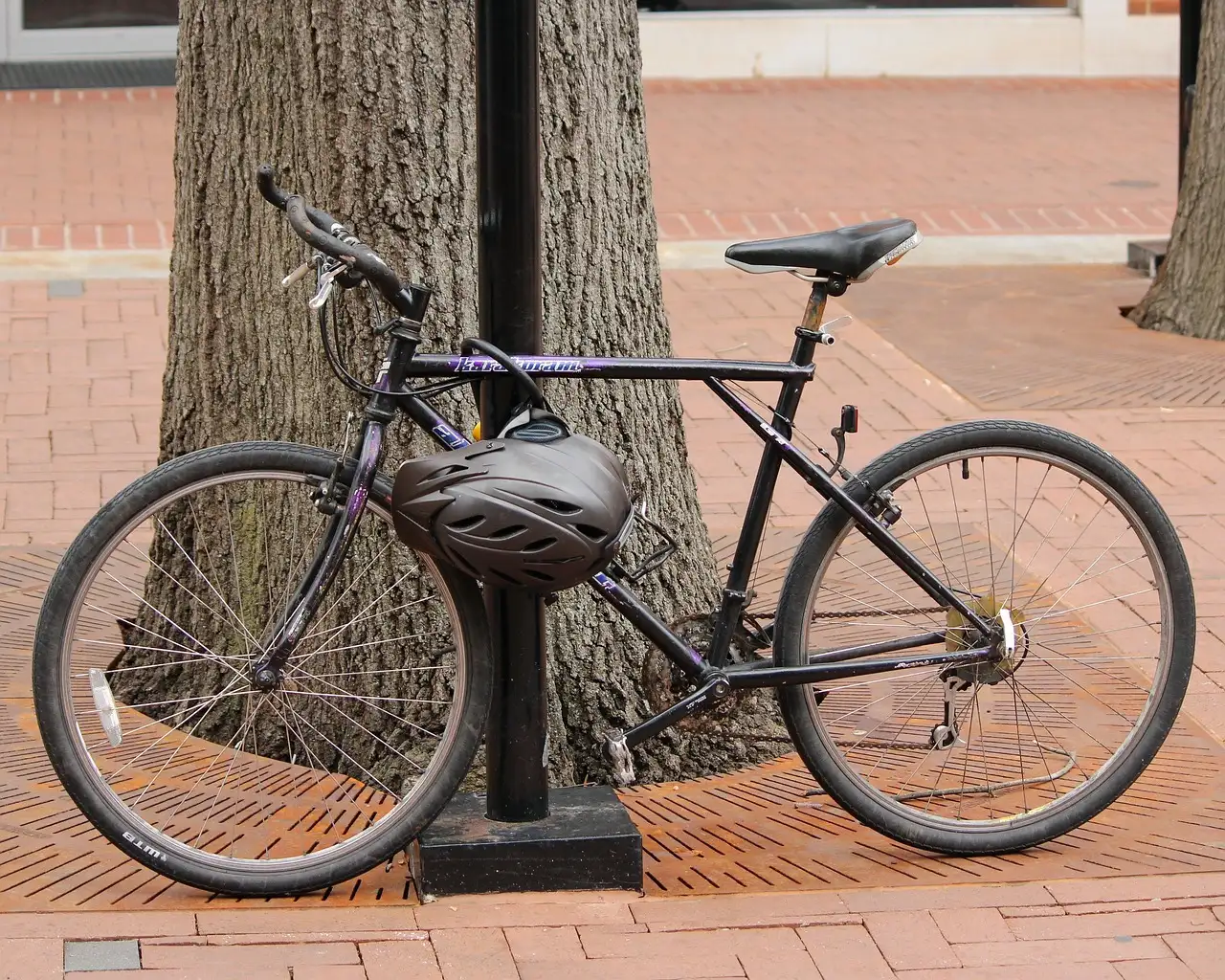 A bicycle with a helmet on the handlebars, locked to a pole on a brick sidewalk