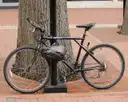 A bicycle with a helmet on the handlebars, locked to a pole on a brick sidewalk