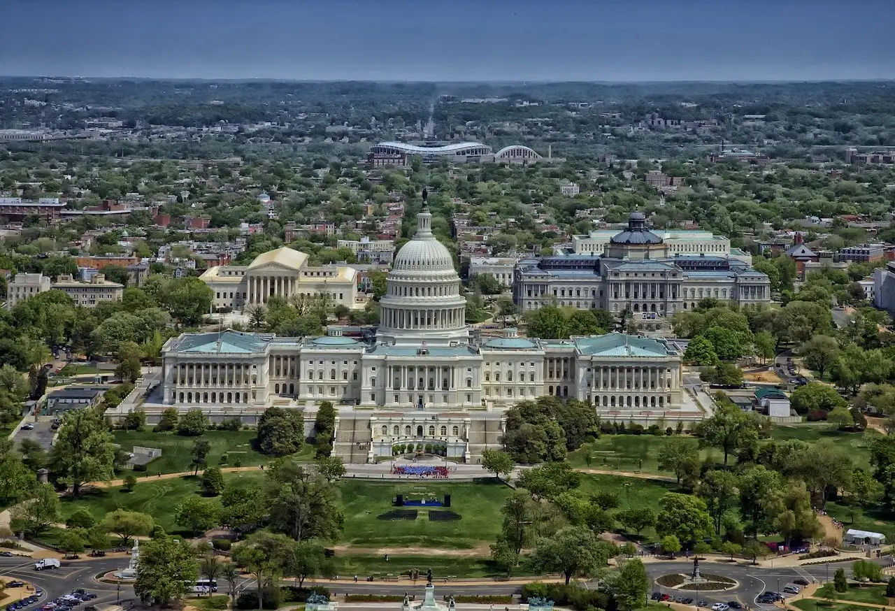 An aerial view of the US Capitol and the green grounds around it, with the city behind