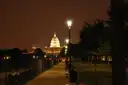 The lit U.S. Capitol dome at night, seen down a path lined with street lamps and trees