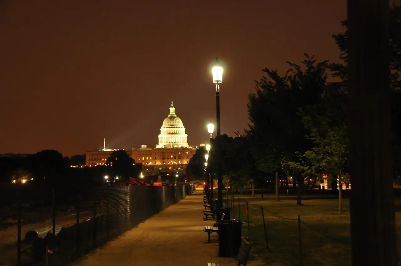 The lit U.S. Capitol dome at night, seen down a path lined with street lamps and trees