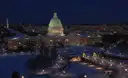 The U.S. Capitol lit up at night above snowy streets, with the Washington Monument in the distance