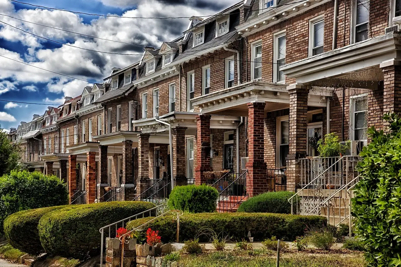 A row of brick row houses with porches and front gardens on a Washington, DC street