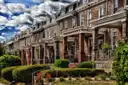 A row of brick row houses with porches and front gardens on a Washington, DC street