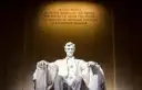 Seated marble statue of Abraham Lincoln lit beneath the carved inscription inside the Lincoln Memorial