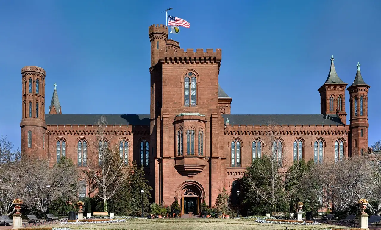 Red sandstone Smithsonian Castle with towers and flag under a blue sky on the National Mall