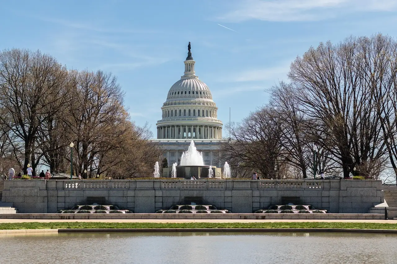 US Capitol dome behind a fountain and reflecting pool, framed by bare trees