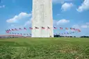 Base of the Washington Monument ringed by American flags on a green lawn