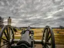 A Civil War cannon looking out over the Gettysburg battlefield on a cloudy day.