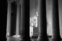 Tall dark columns inside the Lincoln Memorial, with the seated statue of Abraham Lincoln between them, in black and white.