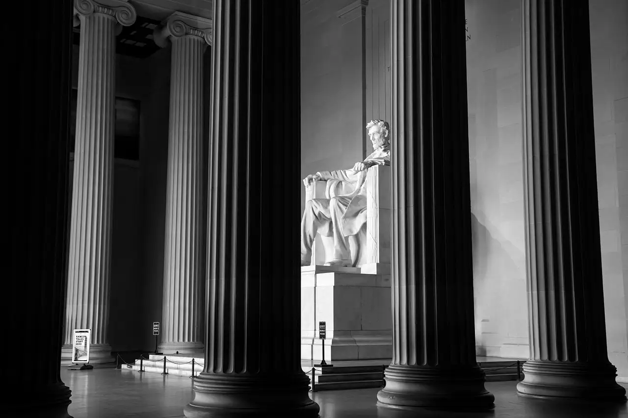 Tall dark columns inside the Lincoln Memorial, with the seated statue of Abraham Lincoln between them, in black and white.