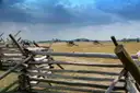 A split-rail fence in the foreground and Civil War cannons on the open battlefield behind it