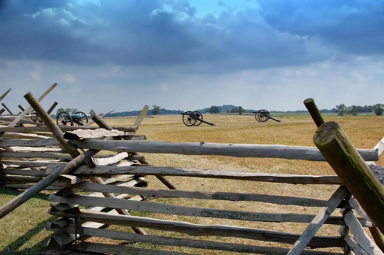 A split-rail fence in the foreground and Civil War cannons on the open battlefield behind it