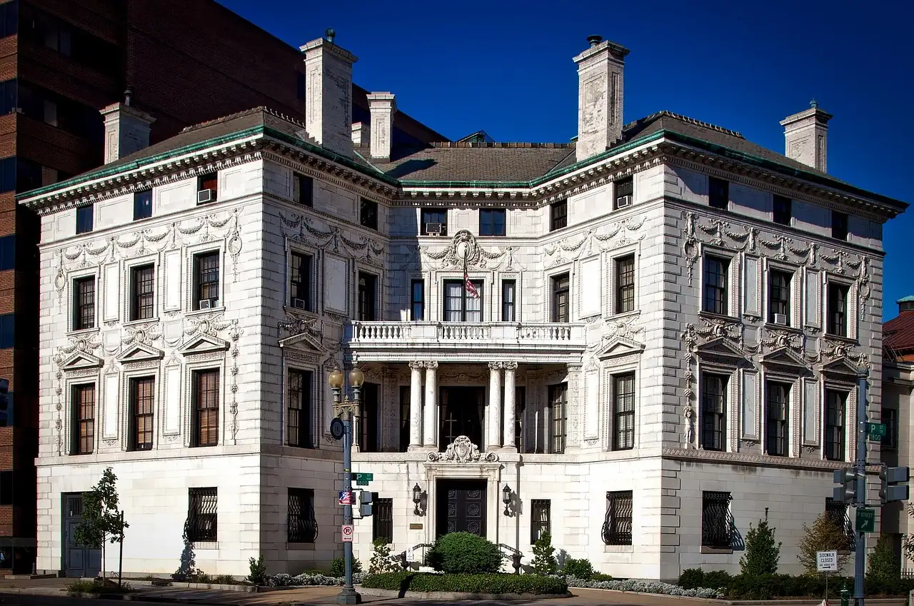 A large white Gilded Age mansion with tall chimneys on a Washington, DC street corner