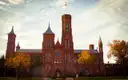 The red sandstone Smithsonian Castle on the National Mall, with autumn trees in front