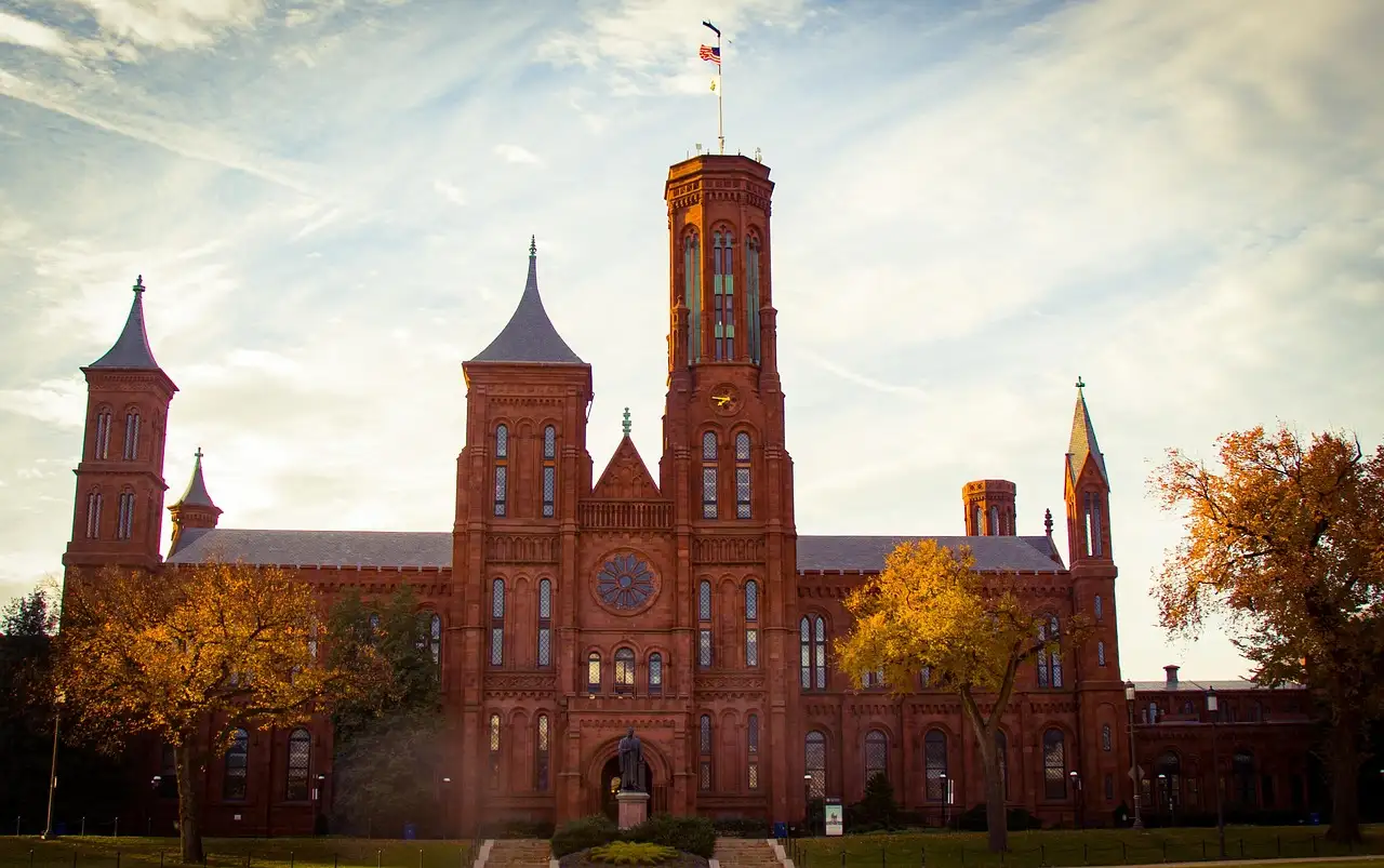 The red sandstone Smithsonian Castle on the National Mall, with autumn trees in front