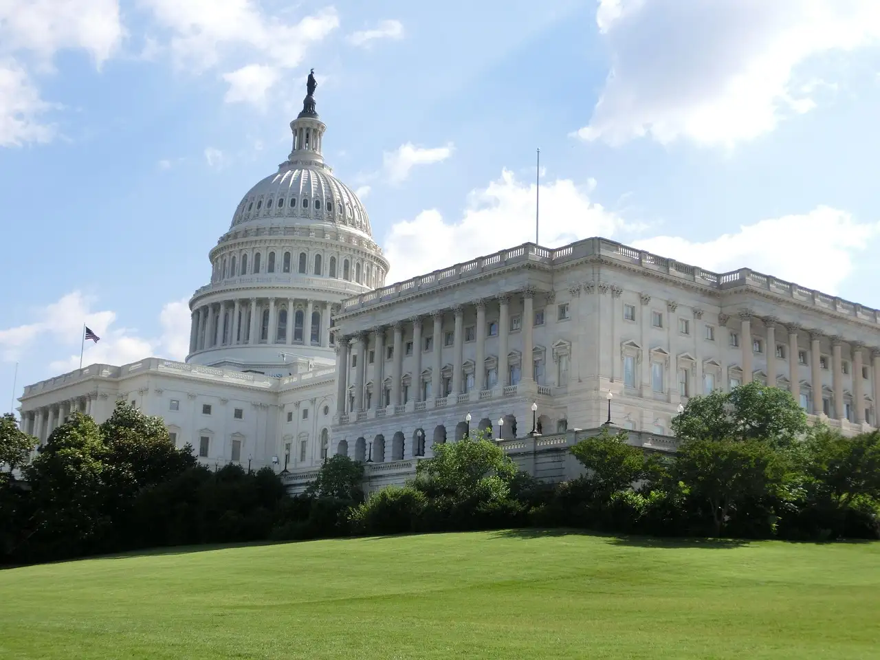 The US Capitol with its white dome above a green lawn and trees