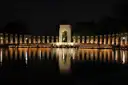 The World War II Memorial lit up at night, its pillars reflected in the pool