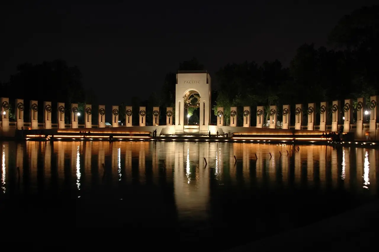 The World War II Memorial lit up at night, its pillars reflected in the pool