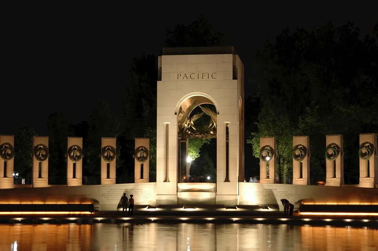 The Pacific arch of the World War II Memorial lit up at night, above the dark pool