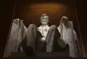 The lit statue of Abraham Lincoln inside the Lincoln Memorial, seen from below
