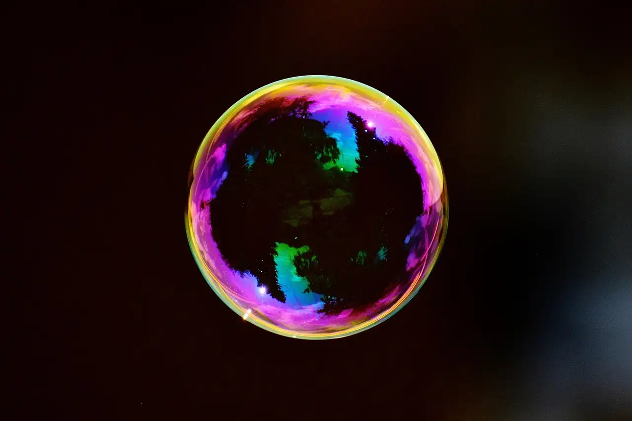 A single soap bubble with rainbow colors floating against a dark background