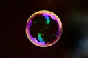 A single soap bubble with rainbow colors floating against a dark background