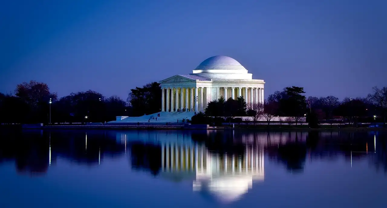 The Jefferson Memorial at dusk, its dome lit and reflected in the still water of the Tidal Basin