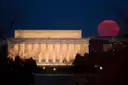 The Lincoln Memorial lit at night, with a red full moon rising beside it