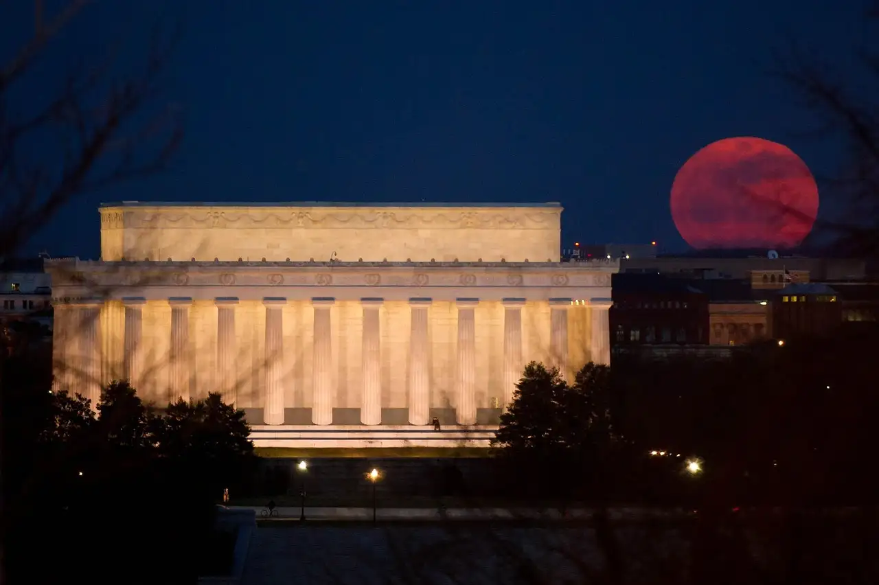 The Lincoln Memorial lit at night, with a red full moon rising beside it