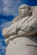 The granite statue of Martin Luther King Jr. at his memorial, arms folded, against a blue sky