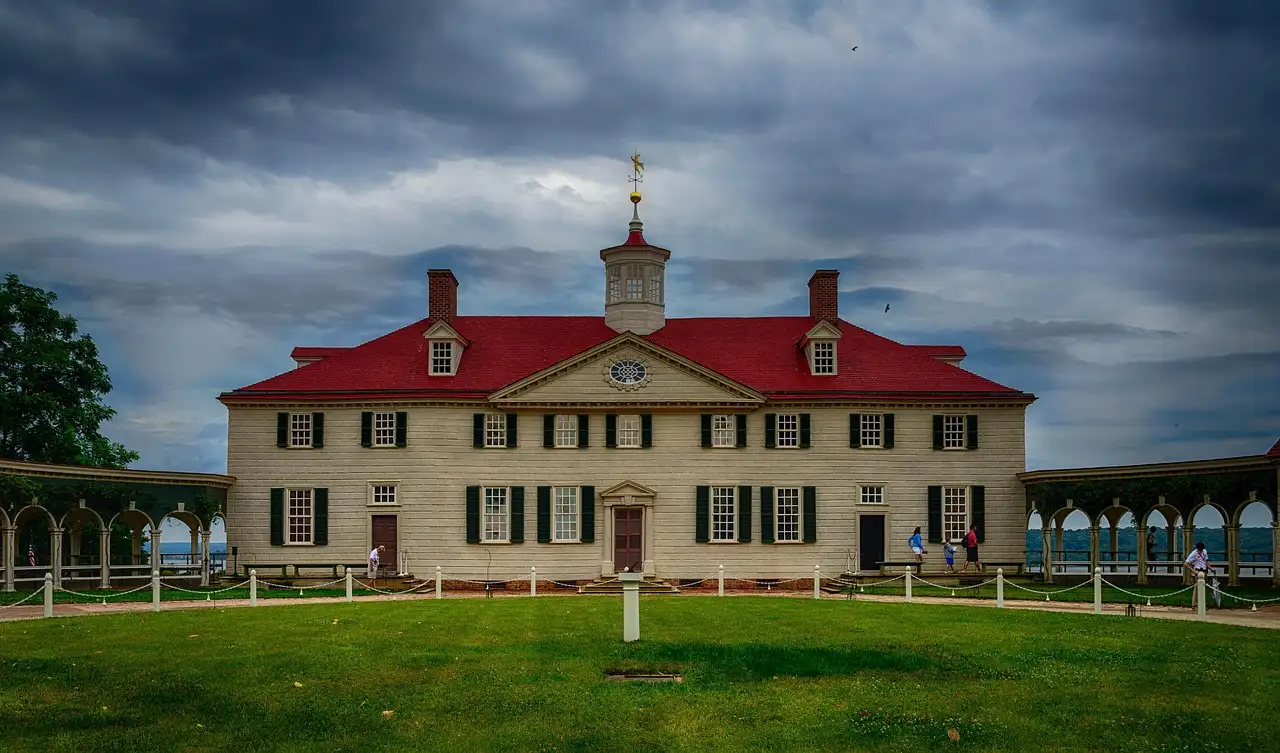 The white Mount Vernon mansion with its red roof and cupola, behind a green lawn under a cloudy sky