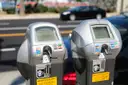 Two grey street parking meters side by side on a city kerb.