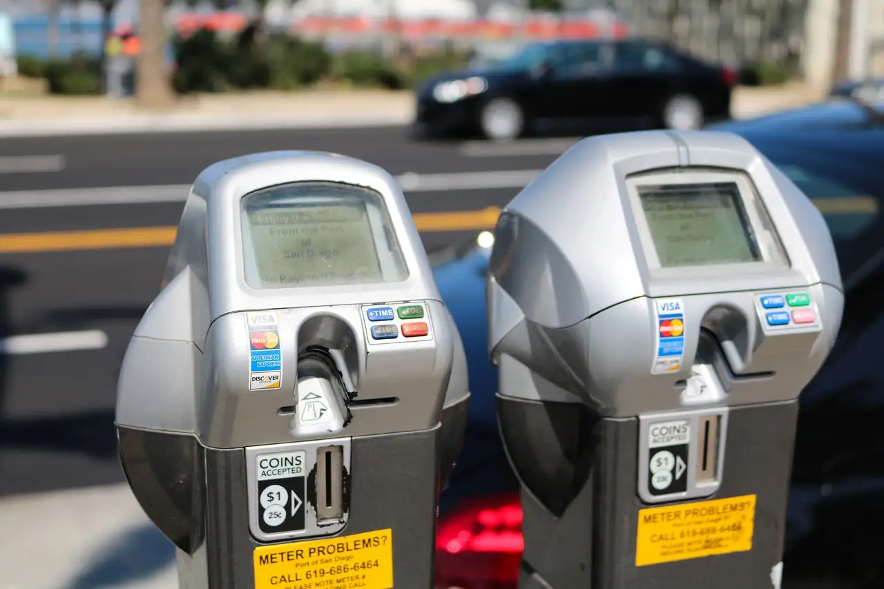 Two grey street parking meters side by side on a city kerb.
