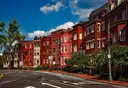 A row of red brick town houses on a street corner under a blue sky