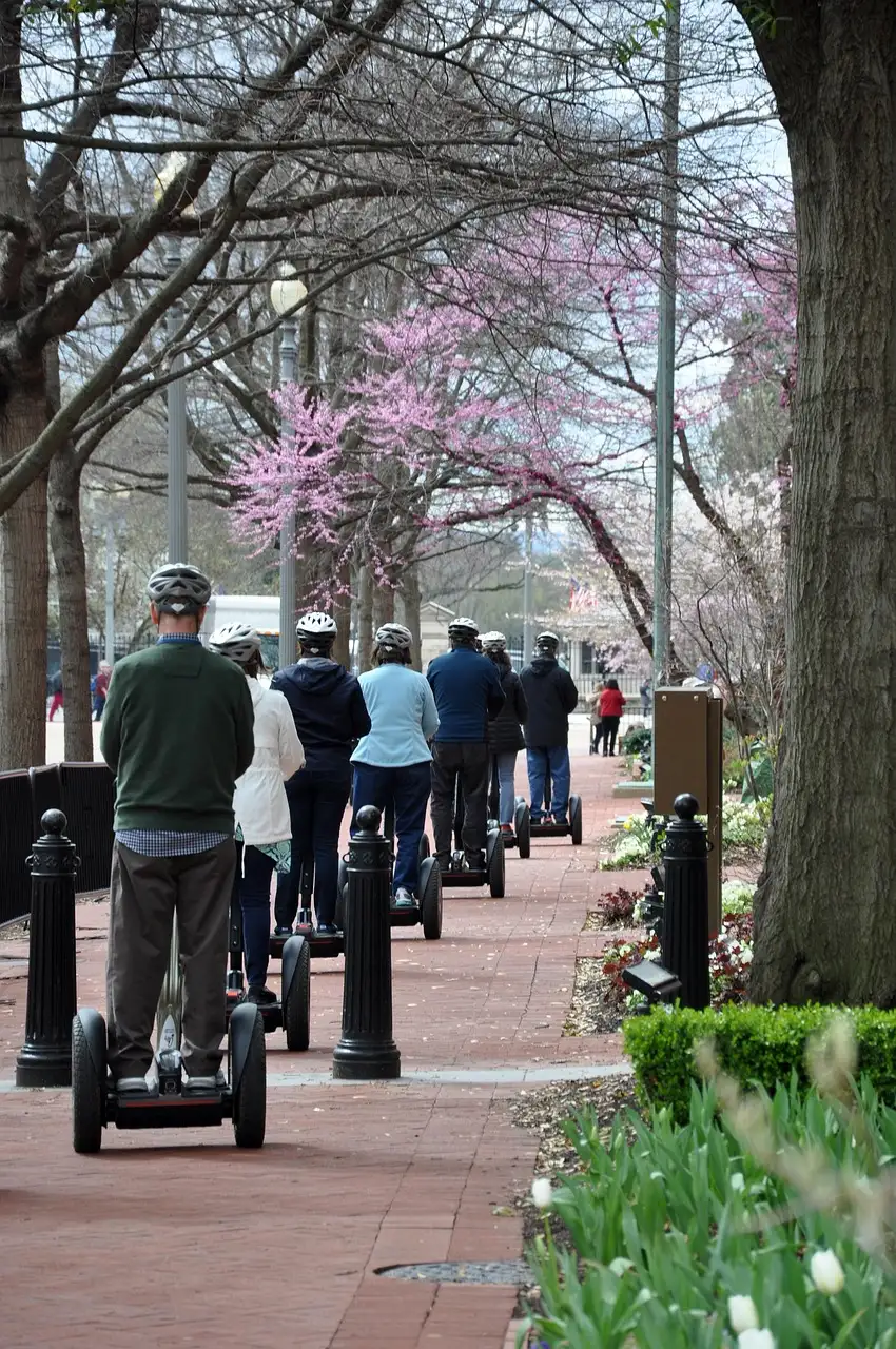 A Segway tour group in helmets riding in single file along a brick sidewalk under spring trees in Washington, DC