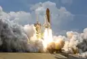 A Space Shuttle lifting off from its launch pad in a cloud of smoke and steam.