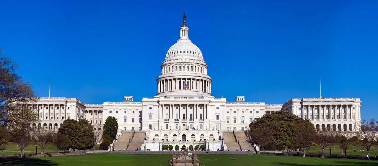 A wide view of the US Capitol with its dome and both wings, behind green lawns