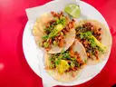 Three tacos with grilled meat, herbs and lime on a white plate