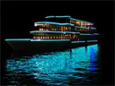 A glass-sided tour boat lit up at night, its lights reflected in the dark water