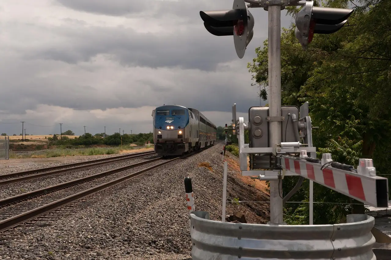 An Amtrak passenger train on a straight stretch of track beside a level crossing under a cloudy sky.