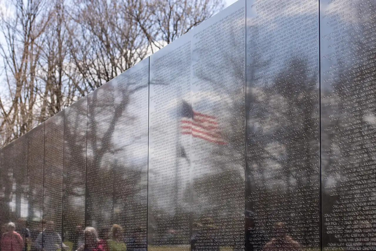 The black granite wall of the Vietnam Veterans Memorial, with names cut into it and an American flag reflected in the stone