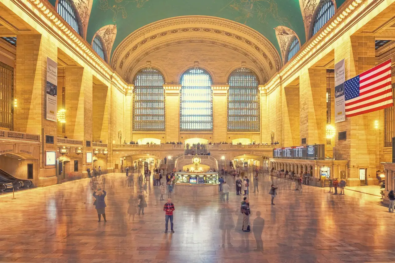 The main concourse of Grand Central Terminal in New York, with its arched windows and a large American flag.