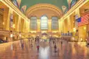 The main concourse of Grand Central Terminal in New York, with its arched windows and a large American flag.