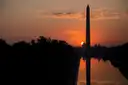 The Washington Monument as a silhouette against an orange sunrise, mirrored in the Reflecting Pool.