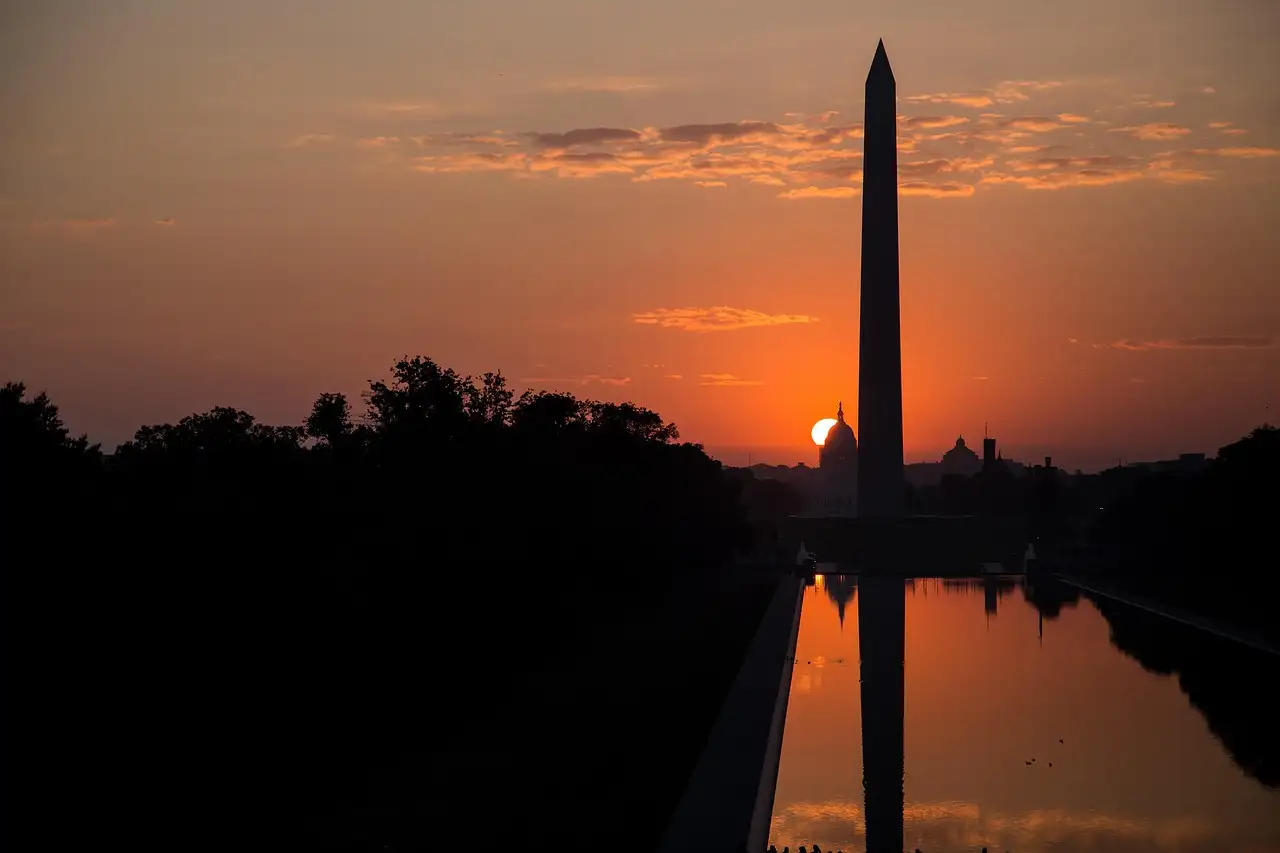 The Washington Monument as a silhouette against an orange sunrise, mirrored in the Reflecting Pool.