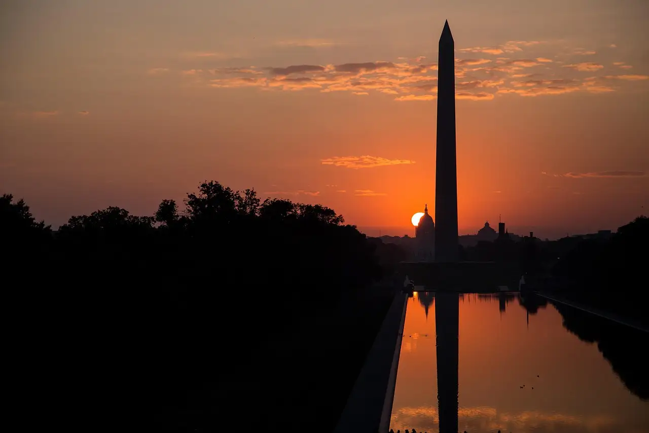 The Washington Monument as a silhouette against an orange sunrise, mirrored in the Reflecting Pool.